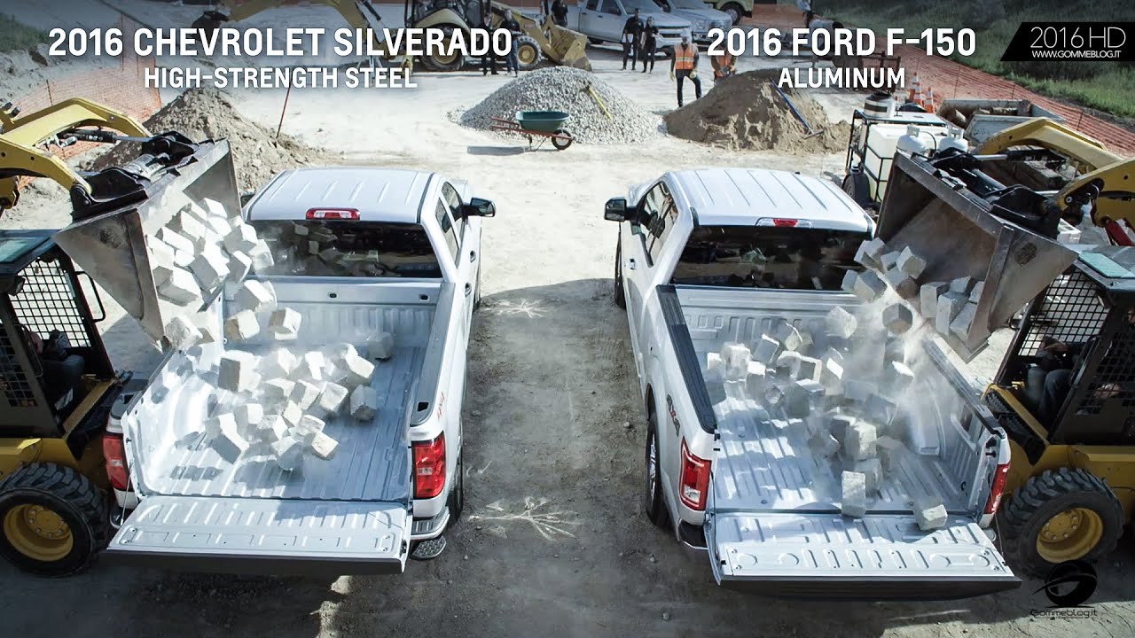 Two pickup trucks side by side as loaders dump concrete blocks into their beds